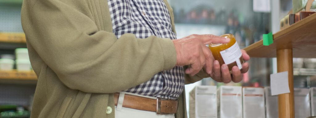Older man reading a product label in a store, illustrating consumer awareness and the importance of clear labeling and compliance in global sleep supplement regulations.
